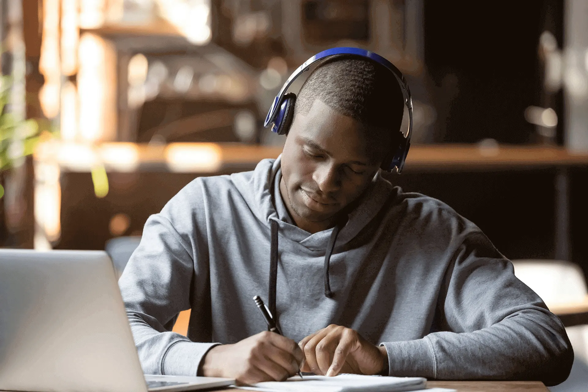 Estudante negro com headphones azuis escrevendo em um caderno
